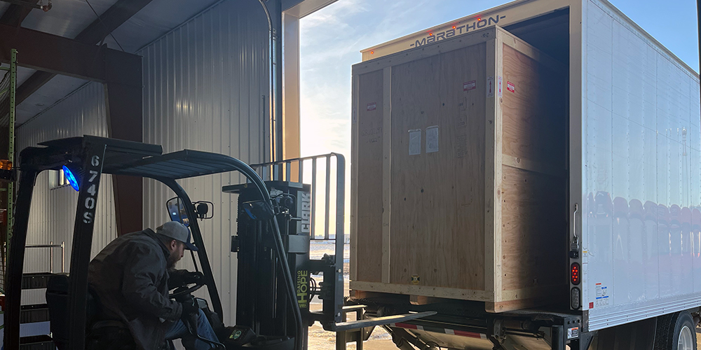 A large crate being unloaded from the trailer of a truck by forklift.